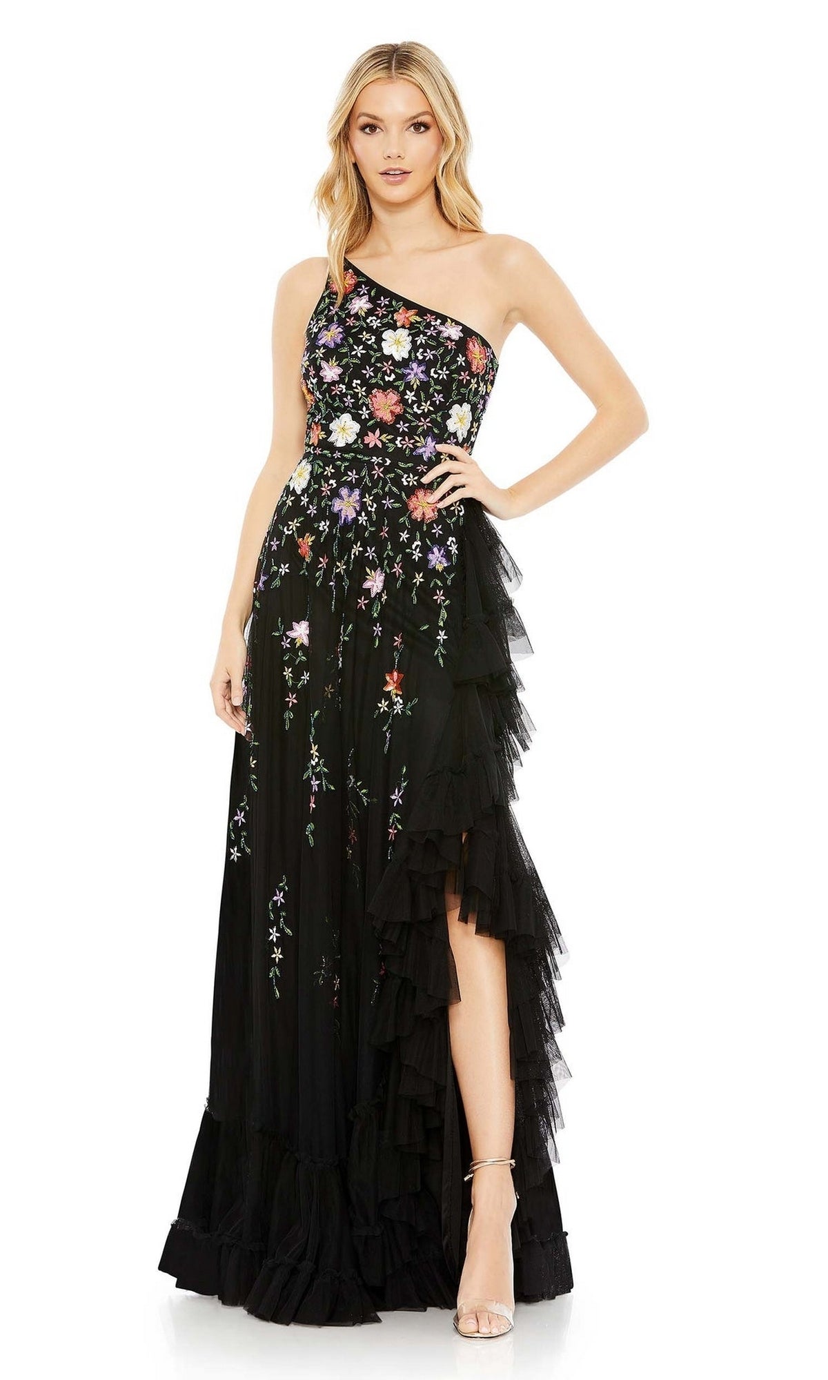 A woman confidently poses with one hand on her hip, wearing the Mac Duggal 9164 One-Shoulder Floral Formal Dress with ruffled layers and elegant embroidery.